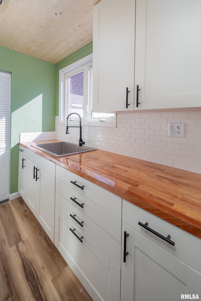 kitchen featuring light wood finished floors, backsplash, white cabinets, a sink, and wood counters