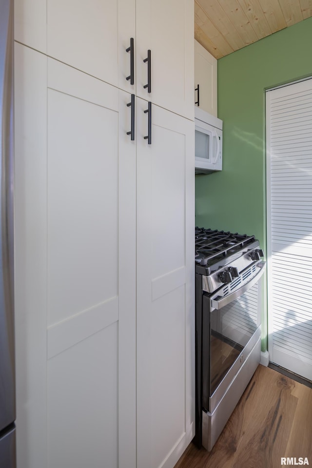 kitchen with white microwave, wood ceiling, wood finished floors, stainless steel gas range, and white cabinetry