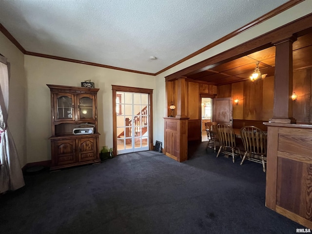 interior space with a textured ceiling, a notable chandelier, ornamental molding, dark colored carpet, and decorative columns