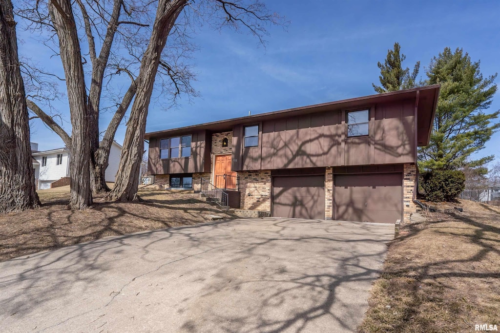 raised ranch with brick siding, central AC, concrete driveway, and a garage