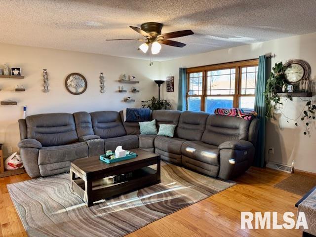 living room with ceiling fan, a textured ceiling, and wood finished floors