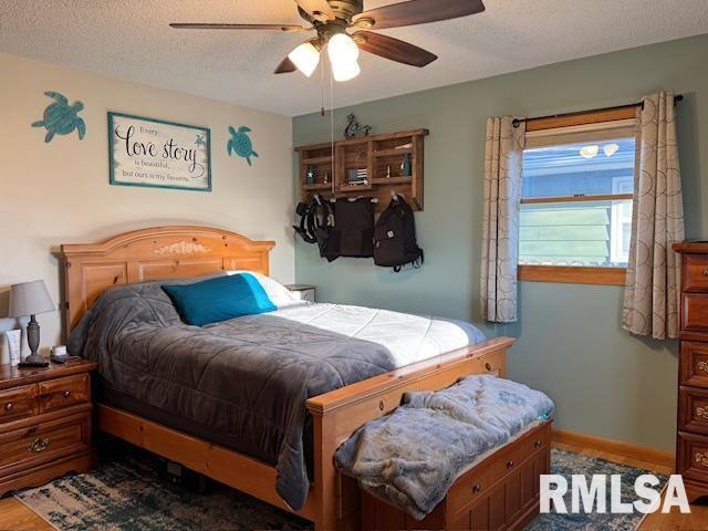 bedroom featuring ceiling fan, baseboards, a textured ceiling, and wood finished floors