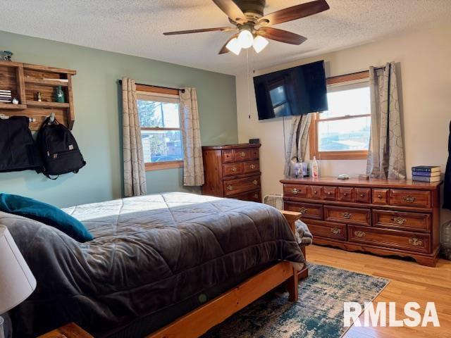 bedroom with light wood-style floors, ceiling fan, and a textured ceiling