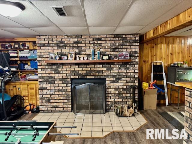 living room with a paneled ceiling, a brick fireplace, wood finished floors, and visible vents