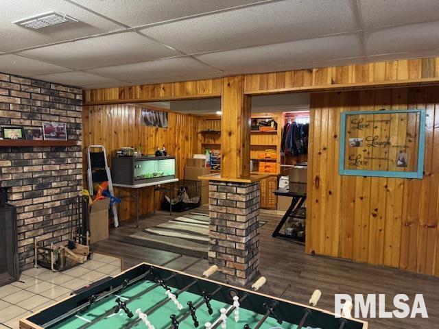 rec room featuring visible vents, a drop ceiling, wooden walls, and wood finished floors