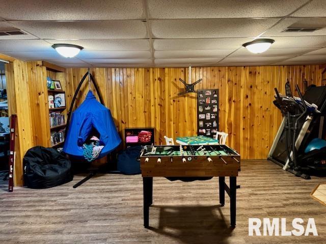 playroom with wood walls, visible vents, a drop ceiling, and wood finished floors