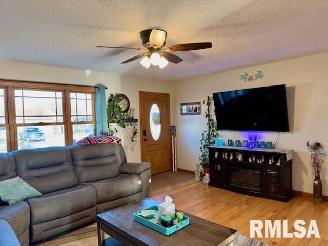 living area with baseboards, ceiling fan, a textured ceiling, and light wood finished floors