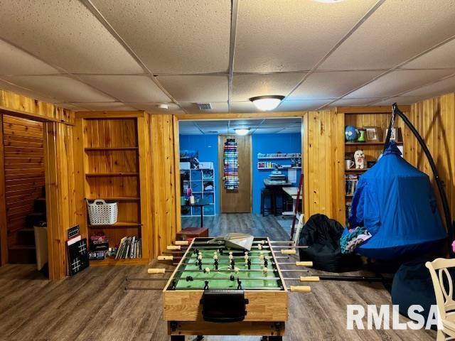 game room featuring a paneled ceiling, wooden walls, and wood finished floors