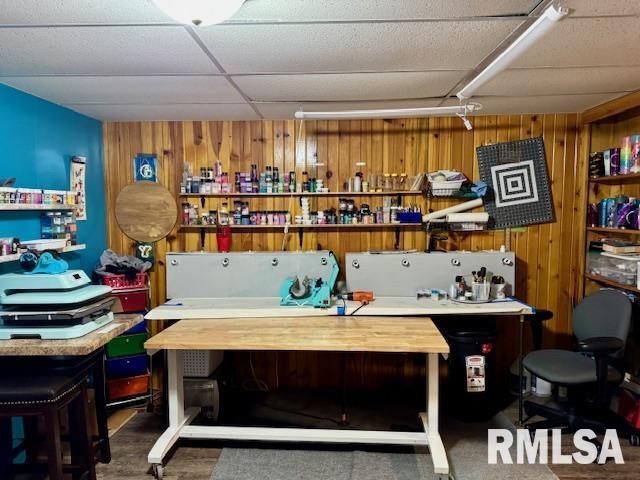 miscellaneous room featuring wooden walls, a drop ceiling, and a workshop area