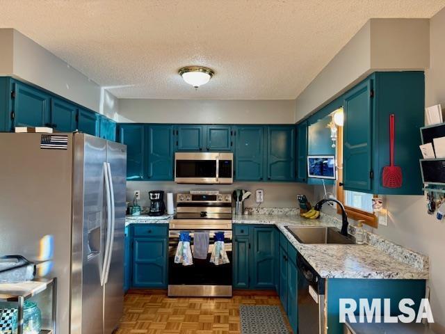 kitchen with a textured ceiling, stainless steel appliances, light stone counters, and a sink