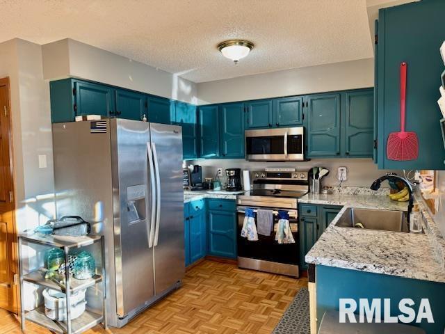 kitchen with a textured ceiling, appliances with stainless steel finishes, a sink, and light stone countertops