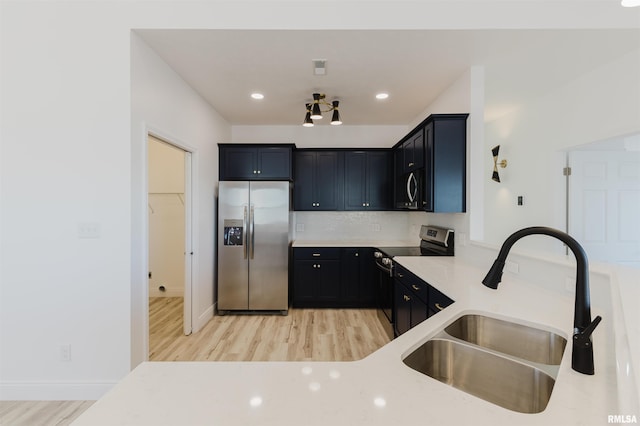 kitchen with a sink, light wood-style floors, appliances with stainless steel finishes, dark cabinetry, and backsplash