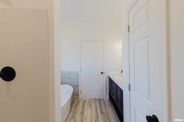 bathroom with a wainscoted wall, wood finished floors, vanity, a freestanding tub, and tile walls