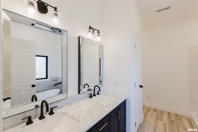 full bathroom featuring visible vents, a sink, a freestanding bath, and wood finished floors