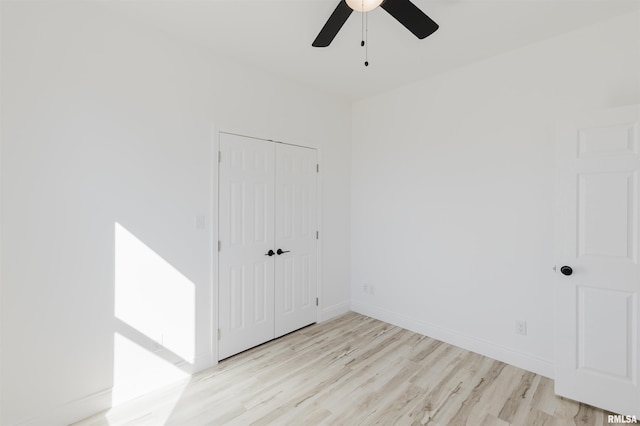 spare room with light wood-type flooring, a ceiling fan, and baseboards