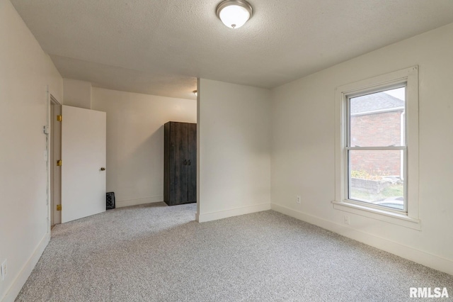 unfurnished room with light colored carpet, baseboards, and a textured ceiling