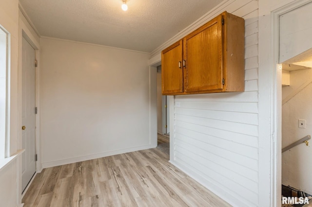 spare room featuring crown molding, baseboards, light wood-type flooring, and a textured ceiling