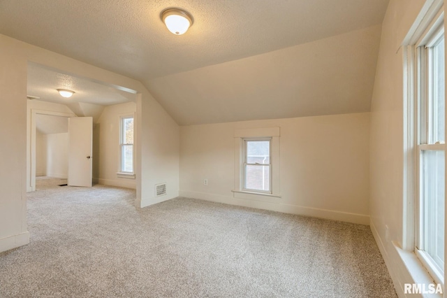 additional living space featuring vaulted ceiling, plenty of natural light, visible vents, and a textured ceiling