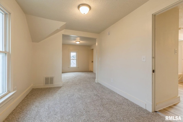 unfurnished room with light carpet, visible vents, a textured ceiling, and baseboards