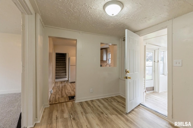 empty room with stairway, light wood-style floors, baseboards, and a textured ceiling