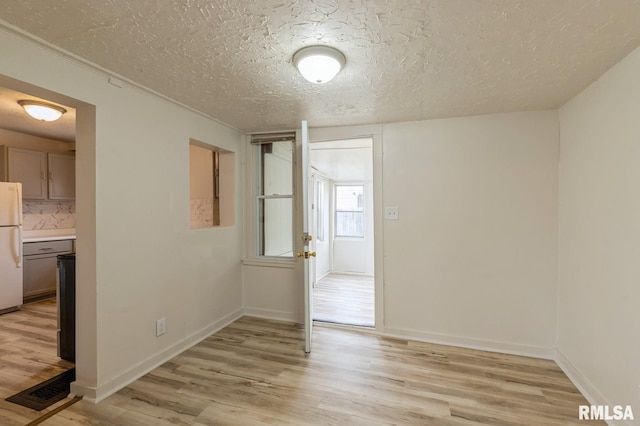 empty room featuring visible vents, baseboards, light wood finished floors, and a textured ceiling