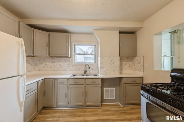 kitchen featuring visible vents, range with gas stovetop, light wood-style flooring, freestanding refrigerator, and a sink