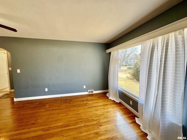 empty room with visible vents, baseboards, wood finished floors, arched walkways, and a ceiling fan