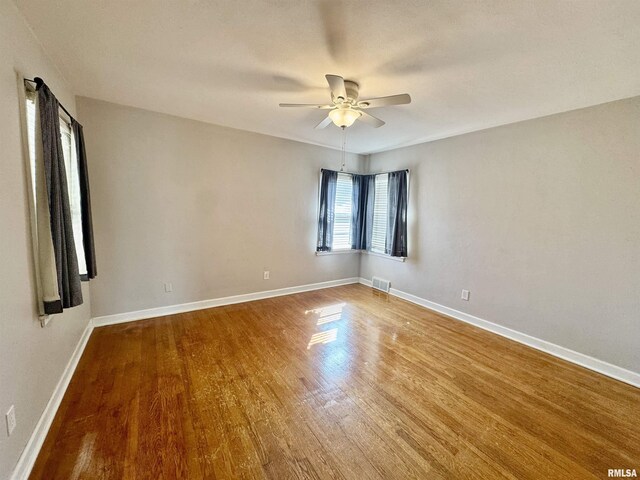 spare room featuring a ceiling fan, wood finished floors, visible vents, and baseboards