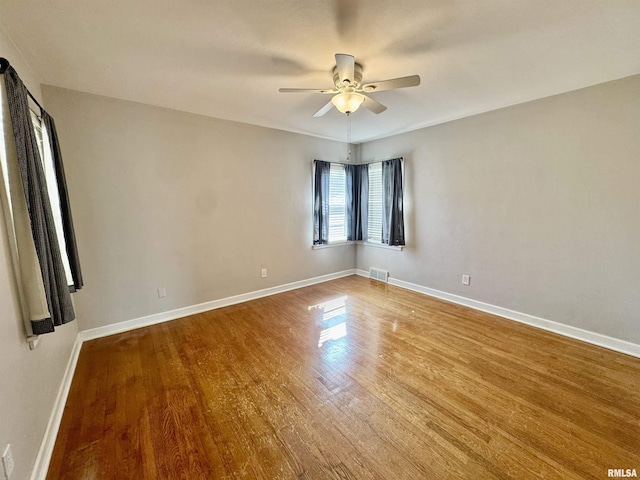 empty room featuring visible vents, a ceiling fan, baseboards, and wood finished floors