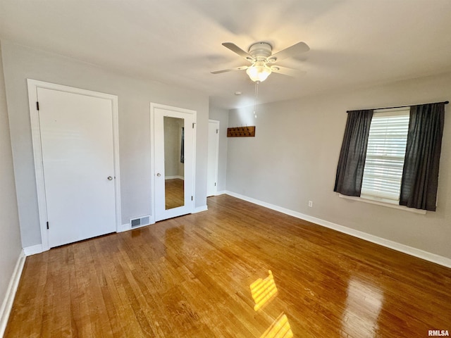 unfurnished bedroom featuring a ceiling fan, wood finished floors, visible vents, and baseboards