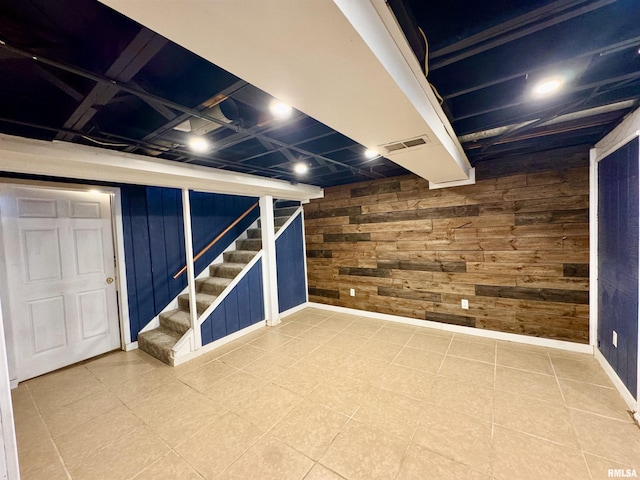 finished basement featuring stairway, baseboards, wooden walls, and visible vents