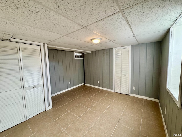 unfurnished bedroom with tile patterned flooring, baseboards, a drop ceiling, and wood walls