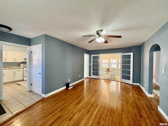 unfurnished living room with ceiling fan, light wood-style floors, arched walkways, and baseboards