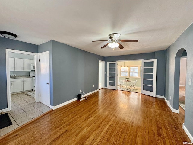 unfurnished living room featuring arched walkways, baseboards, a ceiling fan, and light wood-style floors