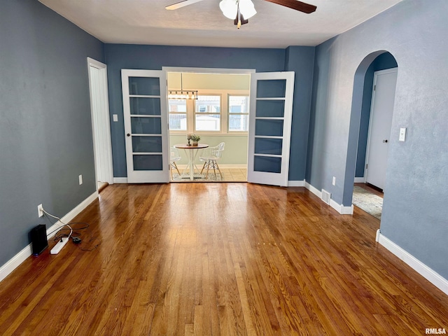 unfurnished room featuring ceiling fan, baseboards, arched walkways, and wood finished floors