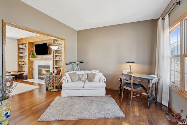 living room with a wealth of natural light, a tile fireplace, and wood finished floors