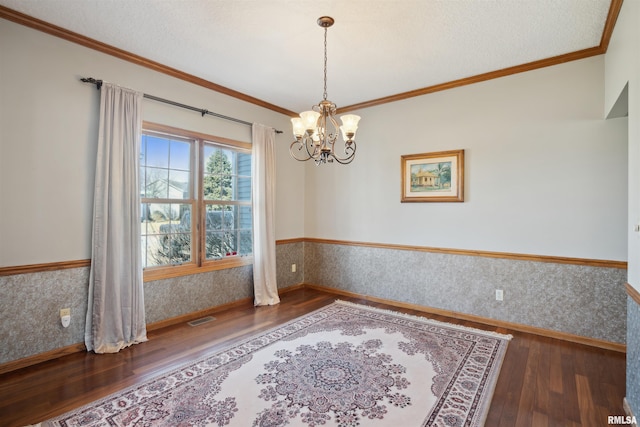 unfurnished room with wood finished floors, a wainscoted wall, wallpapered walls, ornamental molding, and a notable chandelier