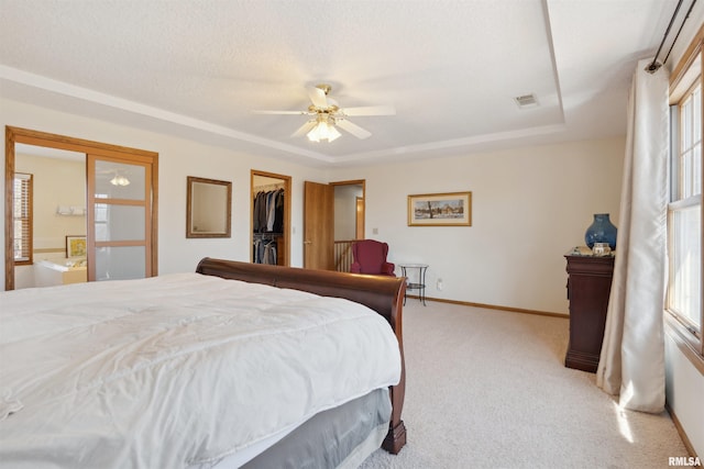 bedroom featuring visible vents, a walk in closet, a raised ceiling, baseboards, and light colored carpet