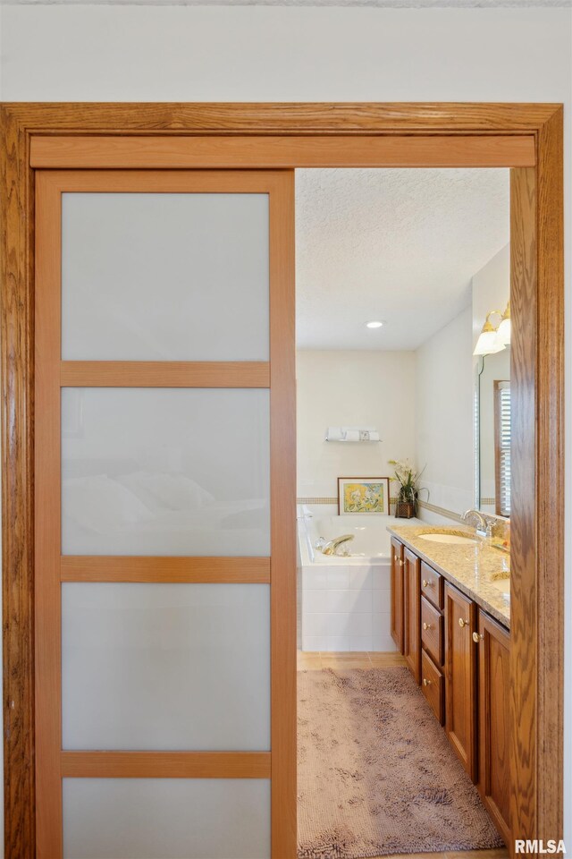 bathroom with a textured ceiling, a garden tub, double vanity, and a sink