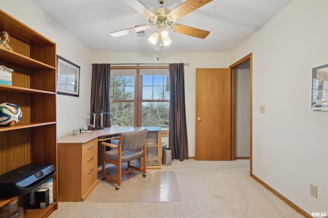 home office with a textured ceiling, a ceiling fan, baseboards, and light carpet