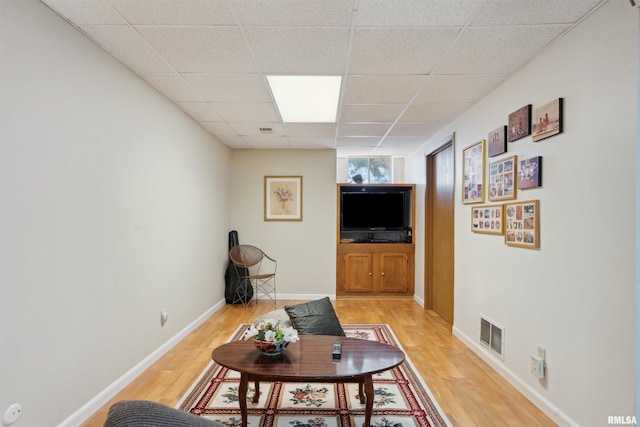 living room featuring a drop ceiling, visible vents, baseboards, and light wood finished floors