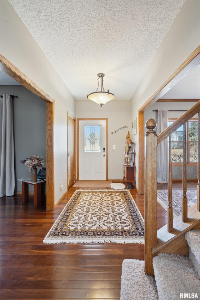 foyer featuring baseboards, a textured ceiling, hardwood / wood-style floors, and stairs