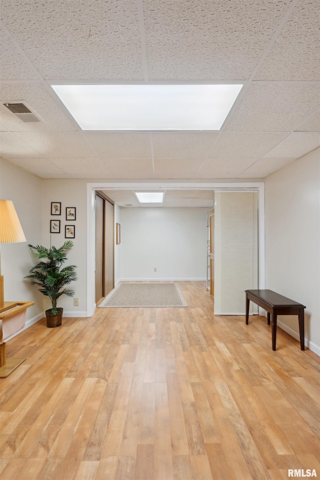 finished basement with wood finished floors, visible vents, a drop ceiling, and baseboards