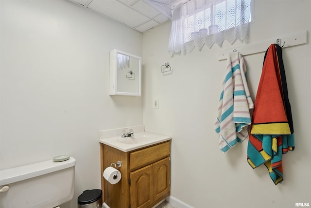 half bathroom with a drop ceiling, toilet, and vanity