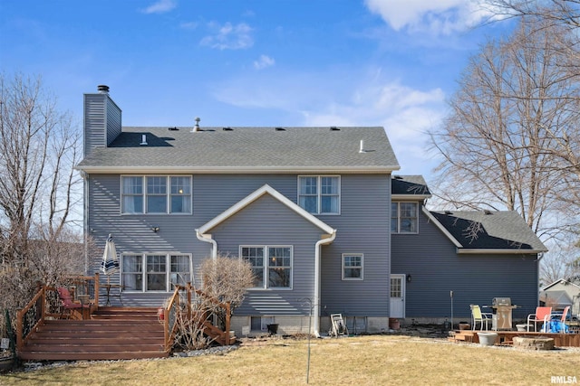 rear view of property featuring a wooden deck, a lawn, roof with shingles, and a chimney