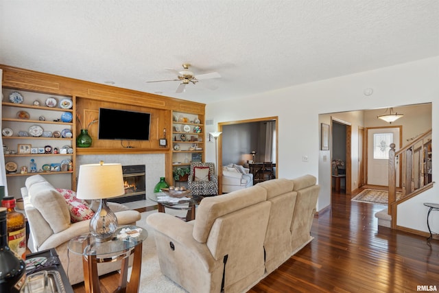 living room with built in features, stairs, hardwood / wood-style flooring, a textured ceiling, and a tiled fireplace