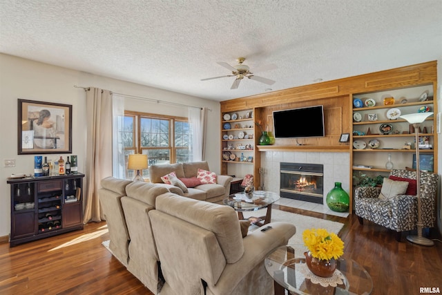 living area featuring built in features, a tile fireplace, a textured ceiling, and wood finished floors