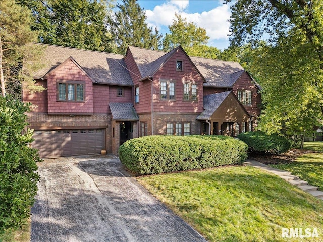 view of front of home with a front yard, driveway, an attached garage, a shingled roof, and brick siding