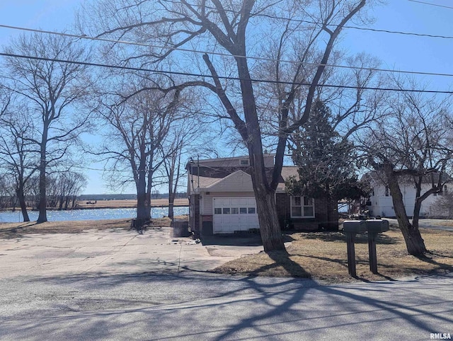 view of front of property featuring brick siding, driveway, a garage, and a water view