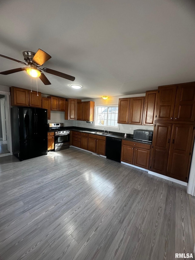 kitchen with black appliances, brown cabinetry, dark countertops, and light wood-type flooring